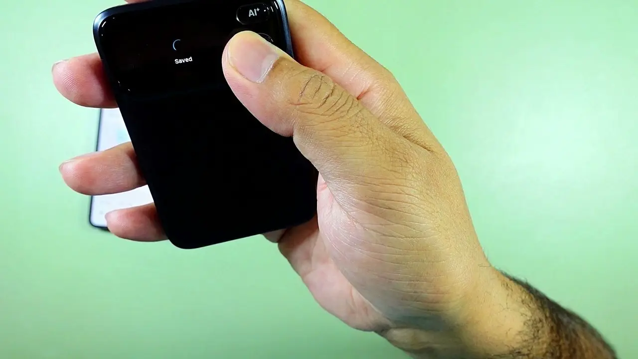 The Comu Action Pro held in a hand with Saved displayed on its OLED screen