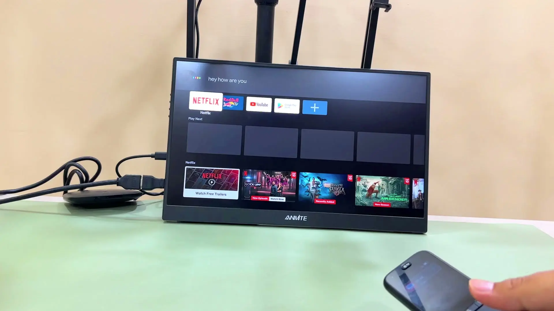 A Google TV screen showing a Google Assistant voice query 'hey how are you' with its response displayed above the home screen apps