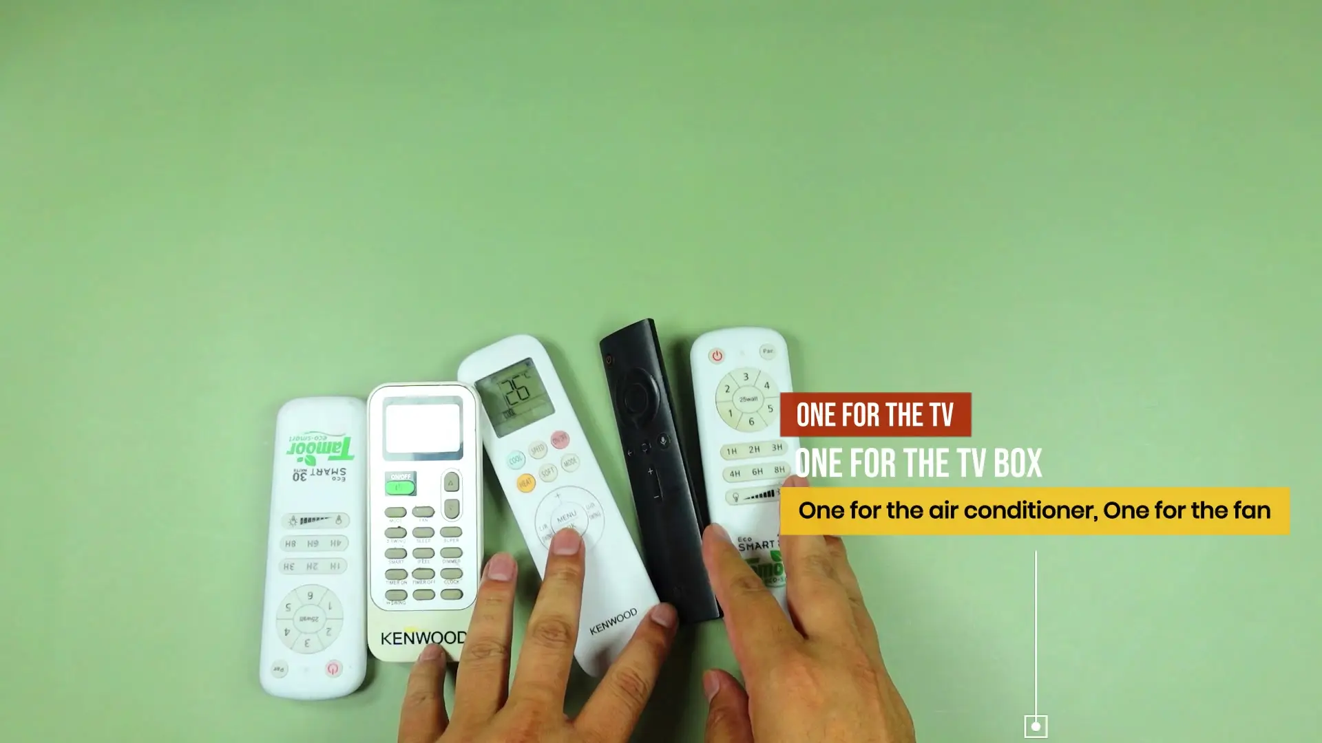 A pile of remotes on a table — a black TV box remote and white remotes for a TV, air conditioner and fan — with on-screen text reading ONE FOR THE TV, ONE FOR THE TV BOX, one for the air conditioner, one for the fan