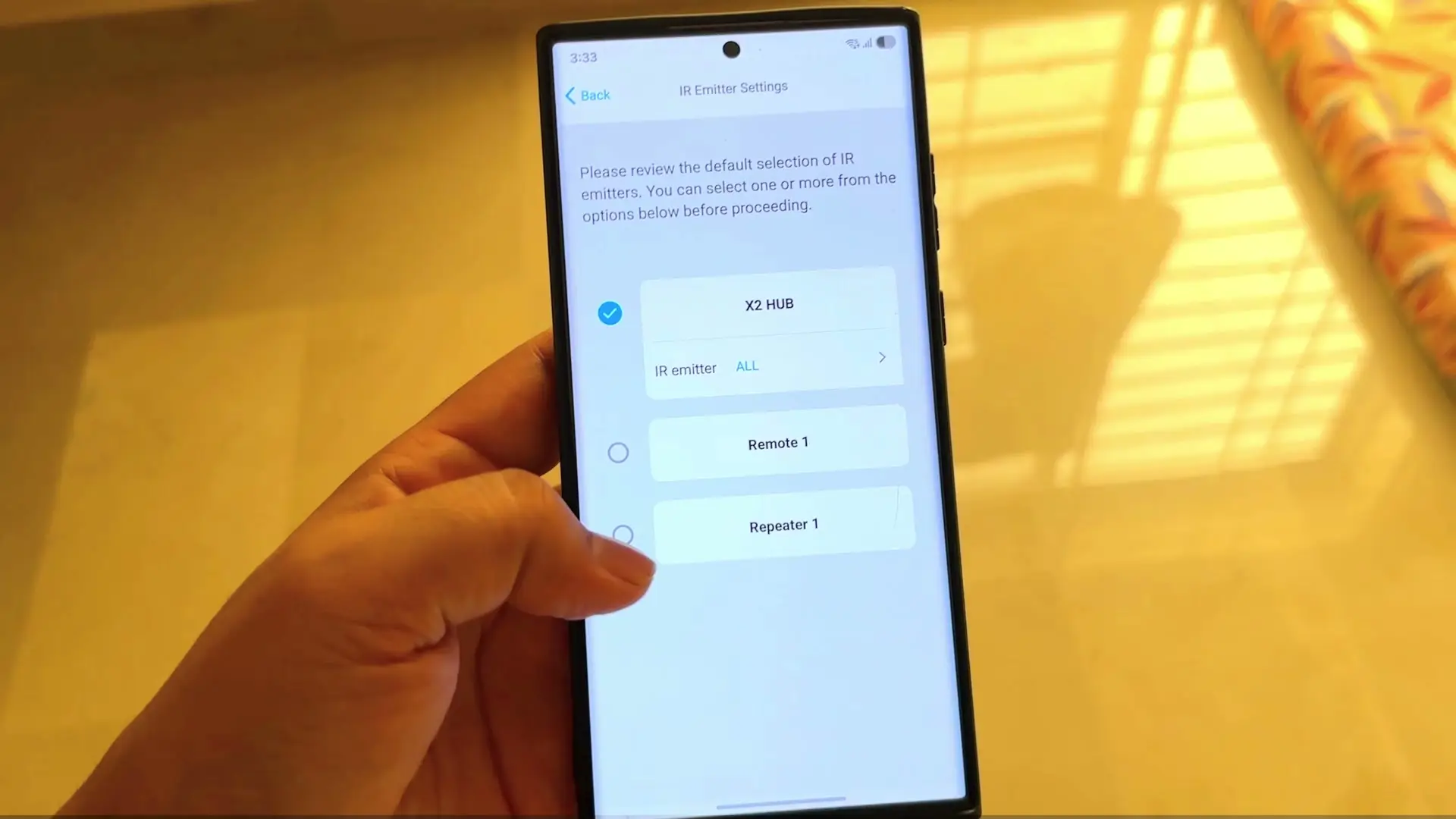 The Sofabaton app's IR Emitter Settings screen on a phone, listing X2 HUB, Remote 1 and Repeater 1 as selectable IR emitters