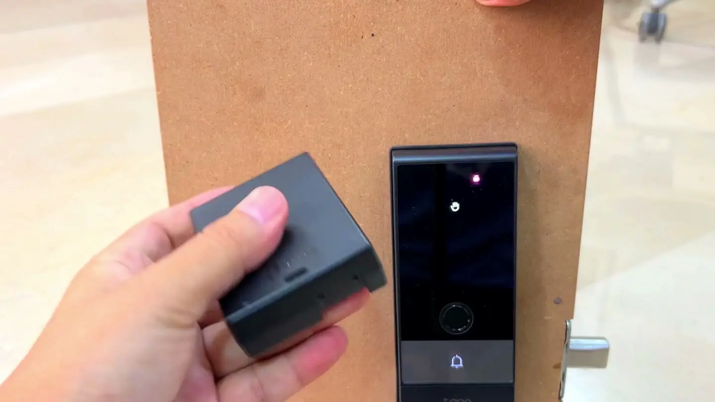 A hand holding the Tapo DL130's removable main battery during backup-power testing