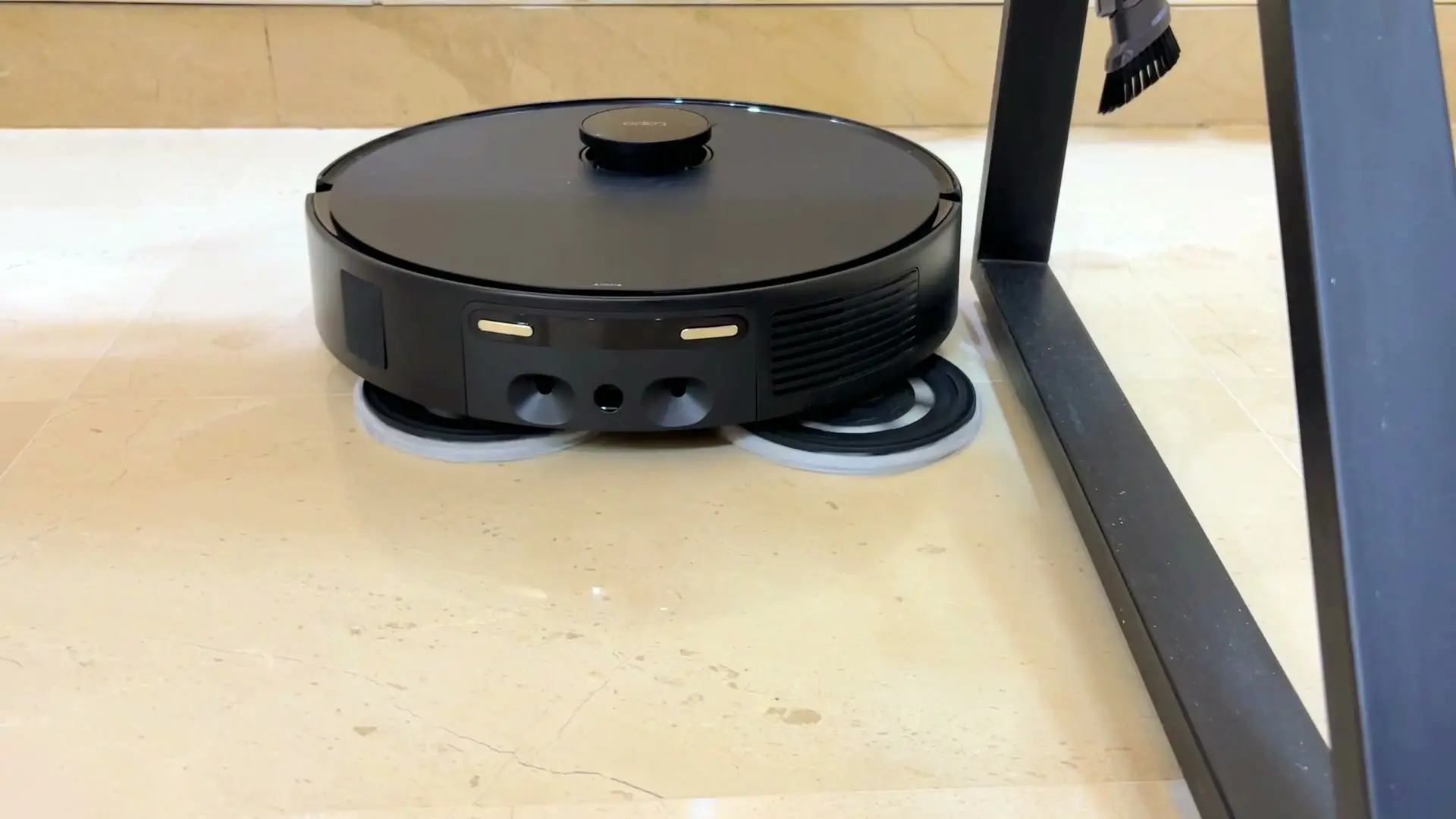 The Tapo RV50 Pro Omni cleaning under a metal table frame on a marble floor, its two round mop pads spinning with visible motion blur