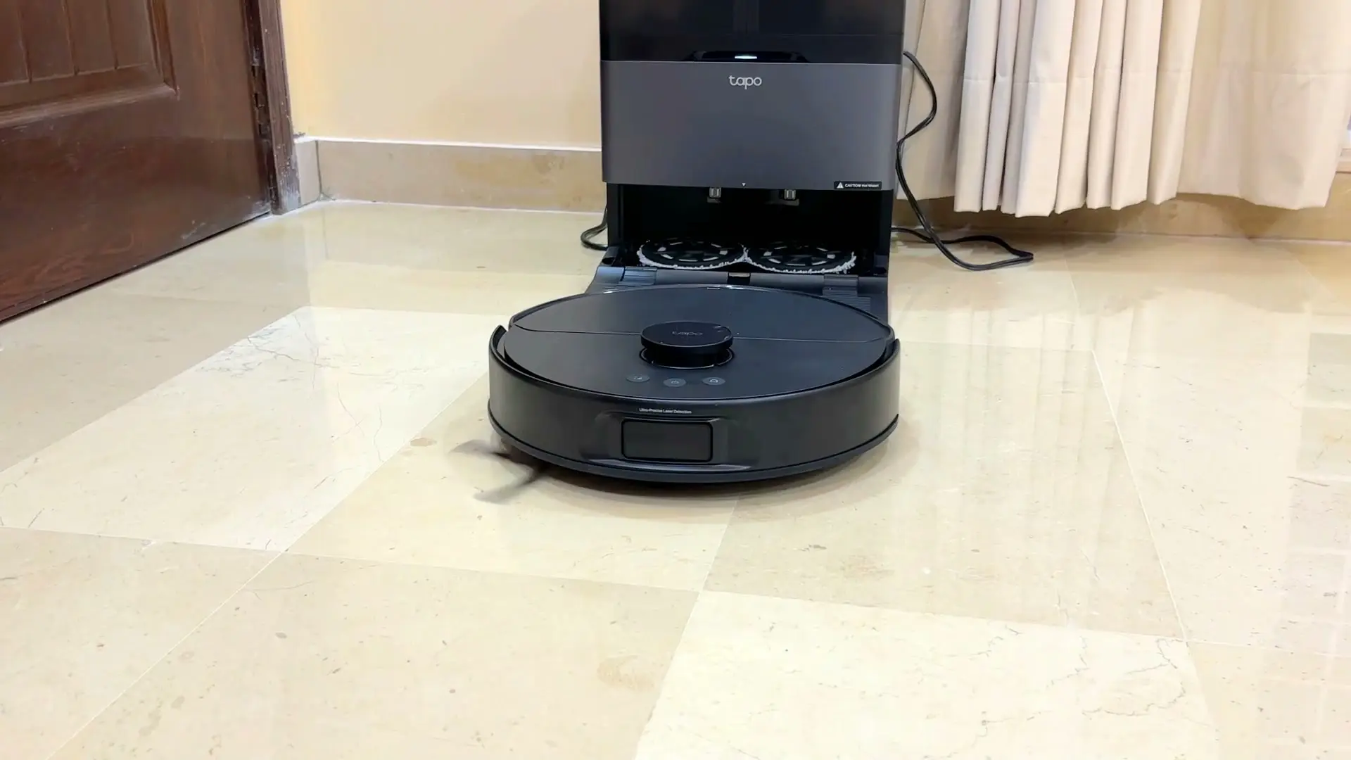 The Tapo RV50 Pro Omni sitting at its dock with the dock flap raised, exposing the two round mop pads underneath in the washing tray