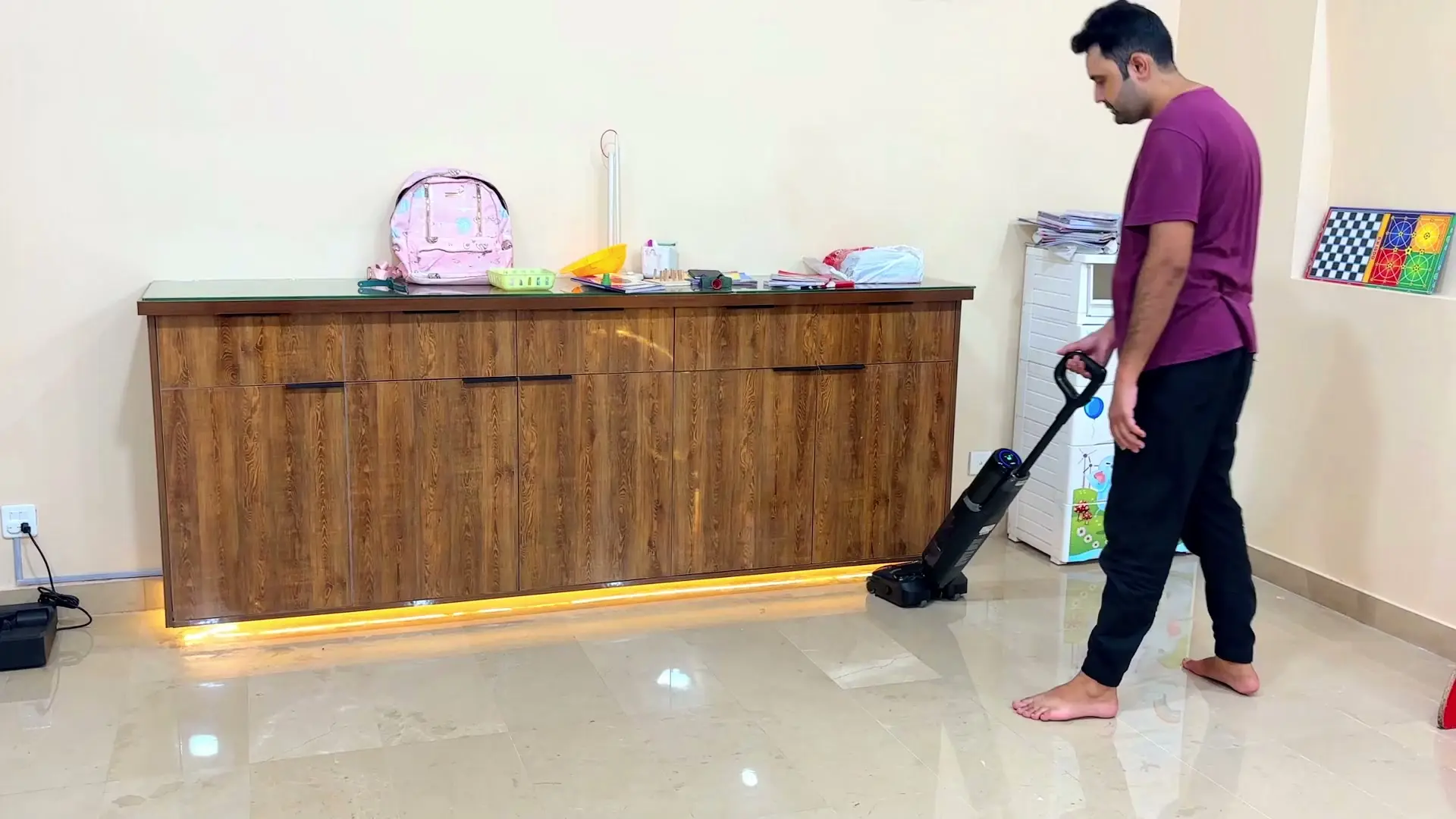 A person walking the upright Tineco floor washer across a marble floor beside a low floating wooden console lit with an LED strip underneath