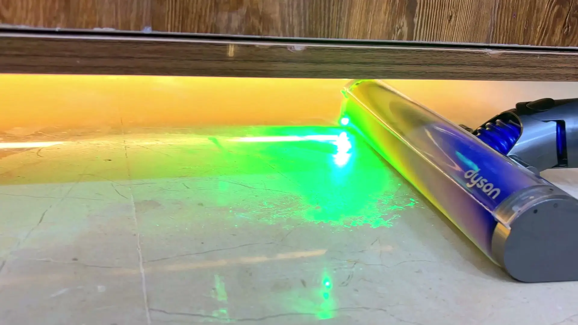 The Dyson V15's green laser casting a bright line across a marble floor, lighting up fine dust in front of the vacuum head