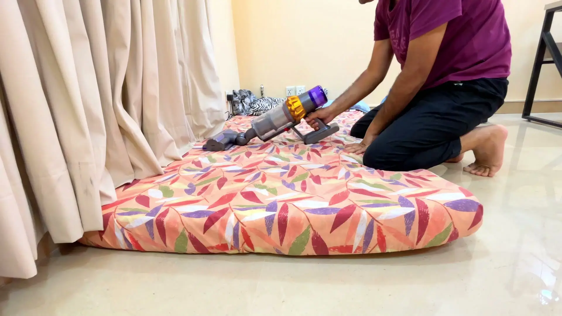 The Dyson V15's motorized cleaner head being pushed across a patterned mattress laid on the floor, with the handheld unit and battery in hand