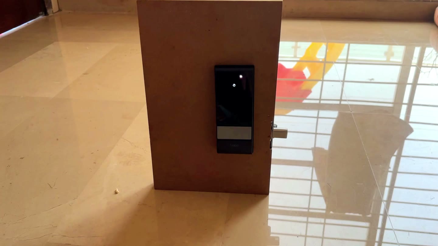 A raised hand in front of the Tapo DL130 during palm-unlock testing, with the palm icon lit on its display
